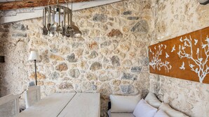 Een rustiek stenen interieur met houten plafond, een hanglamp, een witte lamp en een wandkunstwerk.