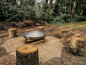 A rustic outdoor setting with a metal cooking pot on a sand base, surrounded by tree stumps.