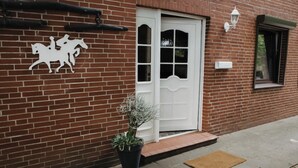 Un edificio de ladrillo con una puerta blanca, la silueta de un caballo, una planta en maceta y una ventana pequeña.