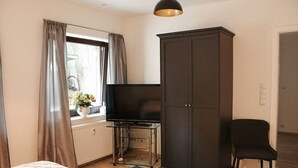 Un dormitorio con cama, televisor en un mueble, armario y una silla.