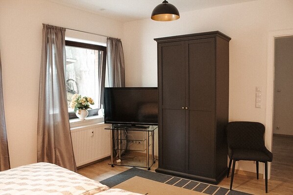 A bedroom with a bed, a TV on a stand, a wardrobe, and a chair.