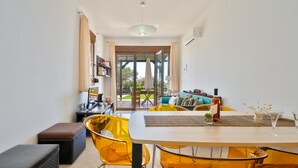 A modern dining area with a wooden table, yellow chairs, and a view of the outdoor seating area. - Smaragdi BeachFront Villa (Asklipeio)