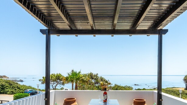 A terrace with a view of the sea, a table with a bottle and glasses, and a pergola overhead. - Smaragdi BeachFront Villa (Asklipeio)