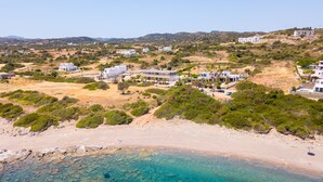 A coastal area with clear turquoise waters, sandy beach, and scattered buildings. - Smaragdi BeachFront Villa (Asklipeio)