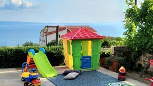A patio with a table set for tea, a play area with a slide, and a view of the sea. - Large 95 m2 apt w. the sea View, Balcony and gar (Podstrana)