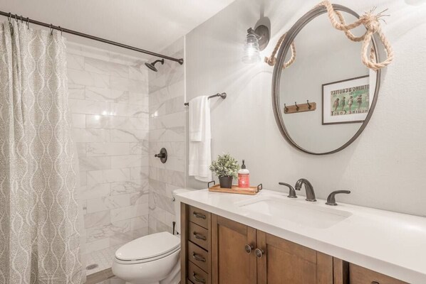 A bathroom with a shower, toilet, vanity with a sink, and a mirror.