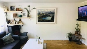 Un salon comprenant un canapé, une table basse, un téléviseur, une bibliothèque et un tableau représentant un paysage, encadré.