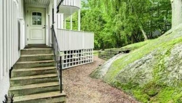Un escalier menant à une porte blanche, entourée de verdure et d’un mur de pierre.