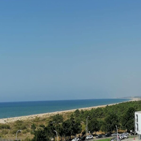 A coastal view with a beach, parked cars, and a building.