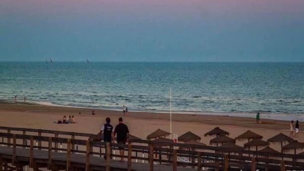 A beach scene with a wooden boardwalk, beach umbrellas, and people relaxing.
