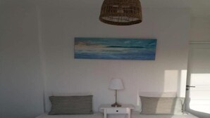 A room with two single beds, a nightstand with a lamp, a painting on the wall, and a wicker hanging light fixture.