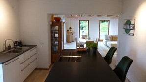 Et moderne køkken med en central ø, et spiseområde med bord og stole, samt udsigt til haven gennem store vinduer.