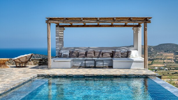 A poolside seating area with a pergola, a cushioned bench, and a wicker chair. - La Bergerie Dantiparos (Antiparos)