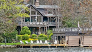 A large, multi-story house with a dock and several white Adirondack chairs. - Beautiful lakefront home nestled into a cove (Lake Toxaway)