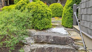 A stone staircase leading to a wooden deck with a railing, surrounded by well-maintained shrubbery and a stone wall. - Beautiful lakefront home nestled into a cove (Lake Toxaway)