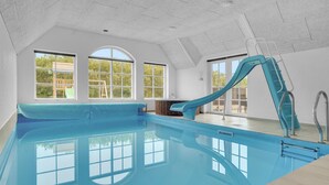 Una piscina interior con tobogán, ventanas amplias y vistas al exterior.