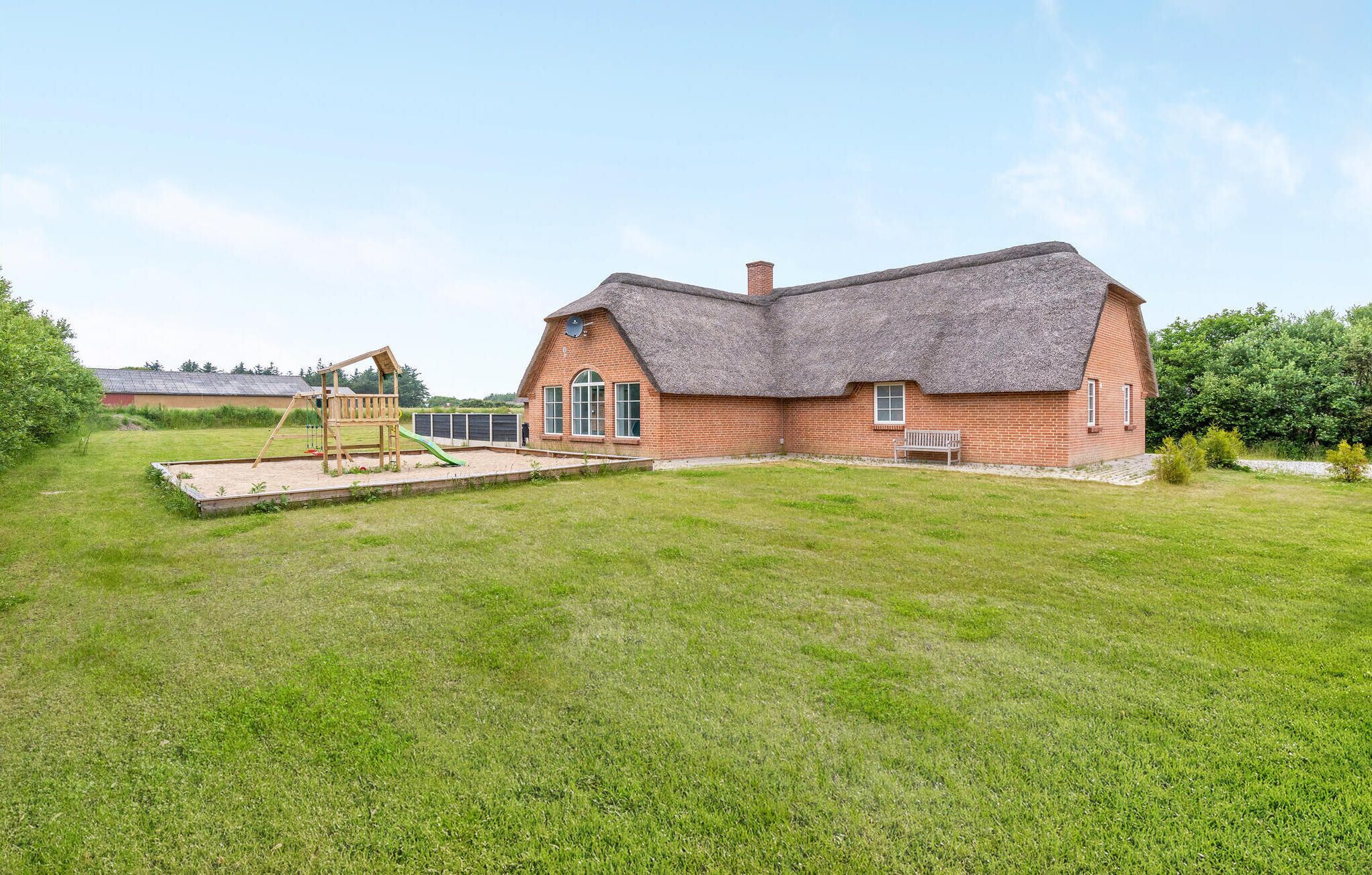 A large brick house with a thatched roof, a wooden play structure, and a well-maintained lawn.