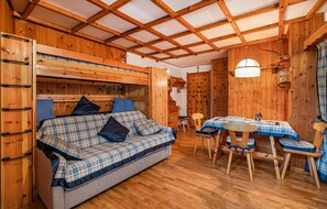 Cozy cabin interior with a comfortable sofa, dining table for two, and wooden ceiling with exposed beams.