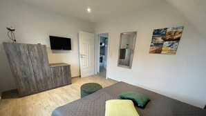 A bedroom with a bed, a wardrobe, a television, and a door leading to another room.