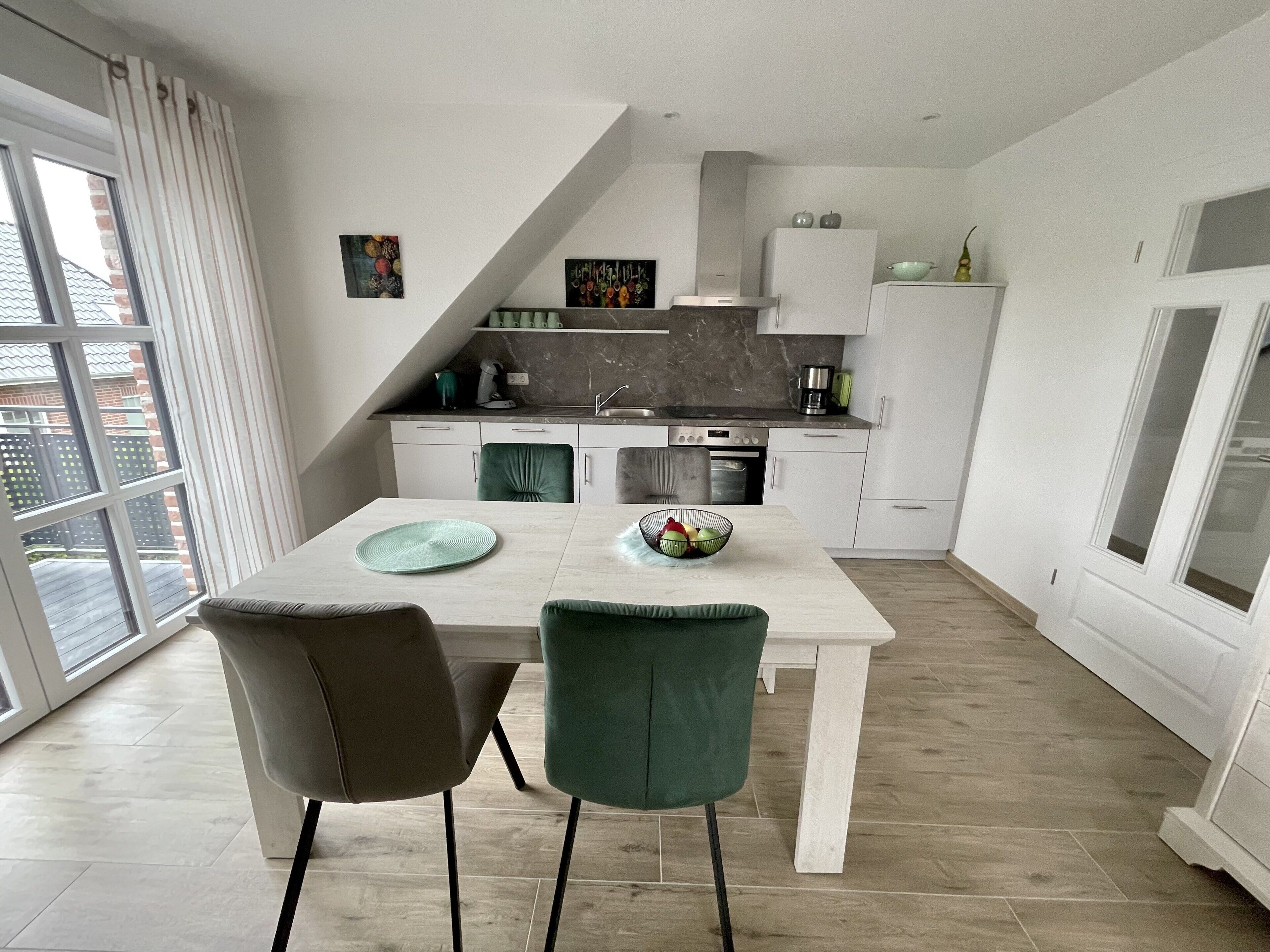 A modern kitchen with white cabinets, a dining table with two chairs, and a view of the outside through a large window.