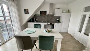 A modern kitchen with white cabinets, a dining table with two chairs, and a view of the outside through a large window.
