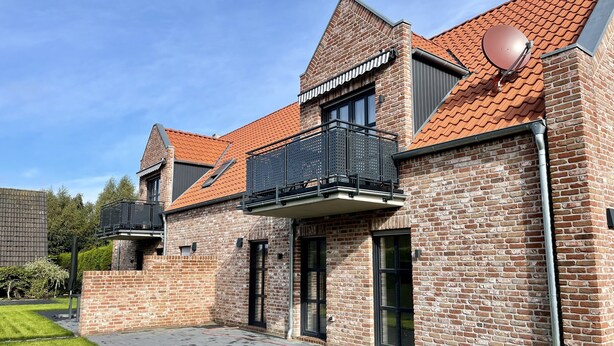A modern brick house with a sloped roof, a balcony with a metal railing, and a satellite dish.