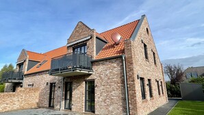 A two-story brick house with a red-tiled roof, a balcony with a metal railing, and a satellite dish.
