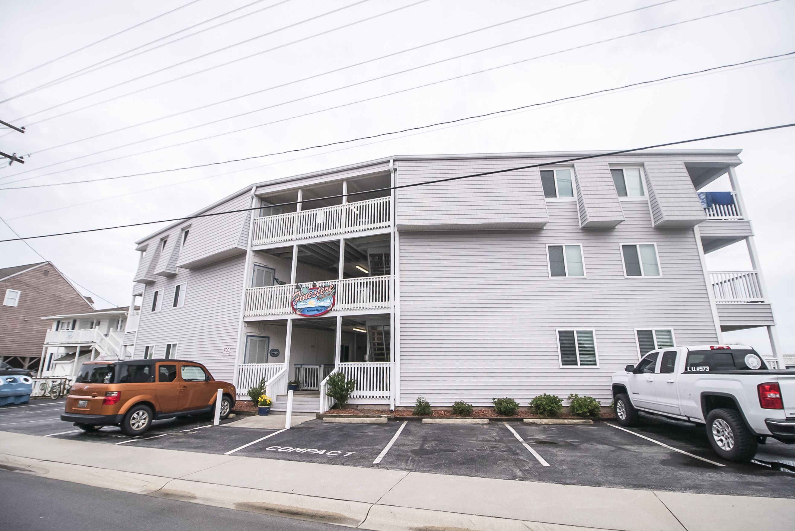 A multi-story building with a balcony on the ground floor, a sign reading "Gracie's," and a parking lot with compact parking spaces.