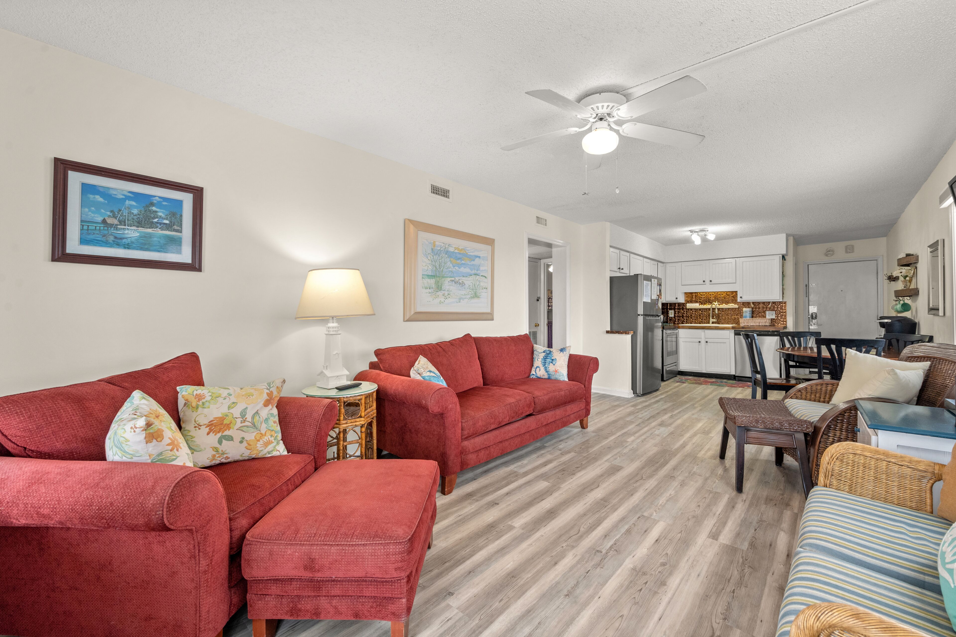 A living room with red sofas, a coffee table, and a dining area with wicker furniture.