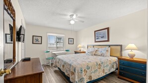 Une chambre à coucher comprenant un lit, un bureau, une chaise, une commode et un ventilateur de plafond.