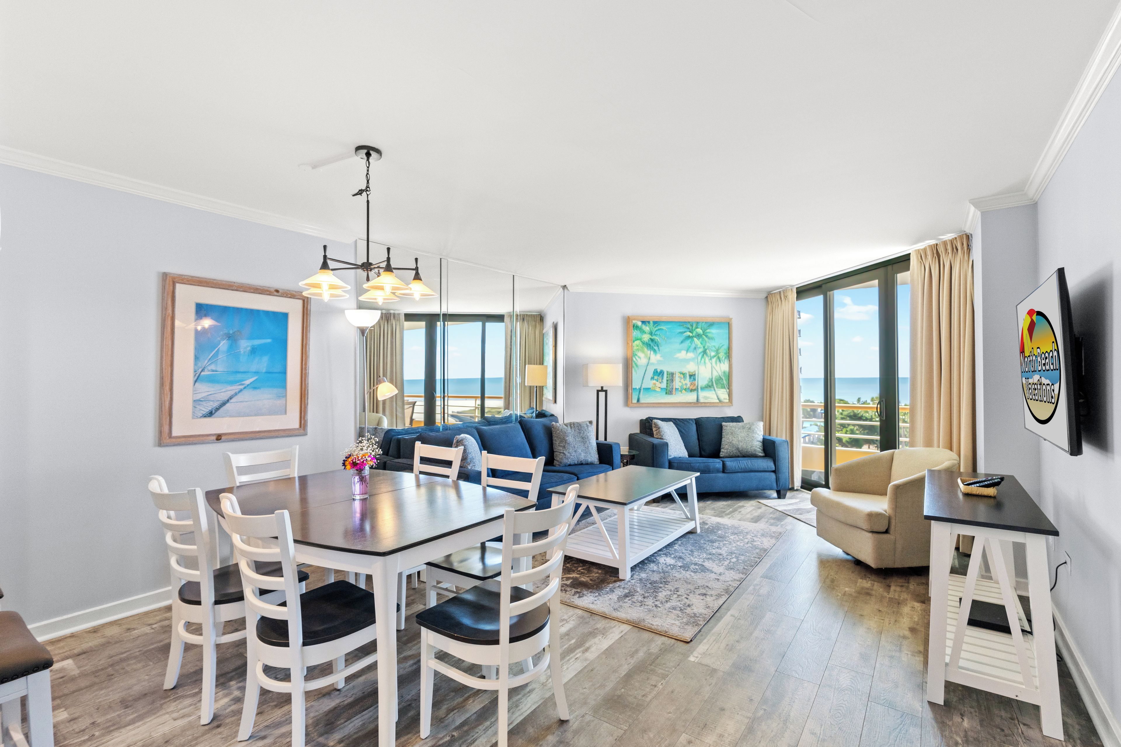 A modern living room with a dining area, large windows, and a view of the ocean.