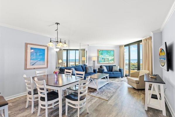 A modern living room with a dining area, large windows, and a view of the ocean.