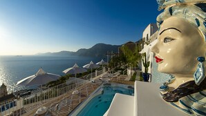 Ett poolområde med parasoller, en bubbelpool och utsikt över havet och bergen.
