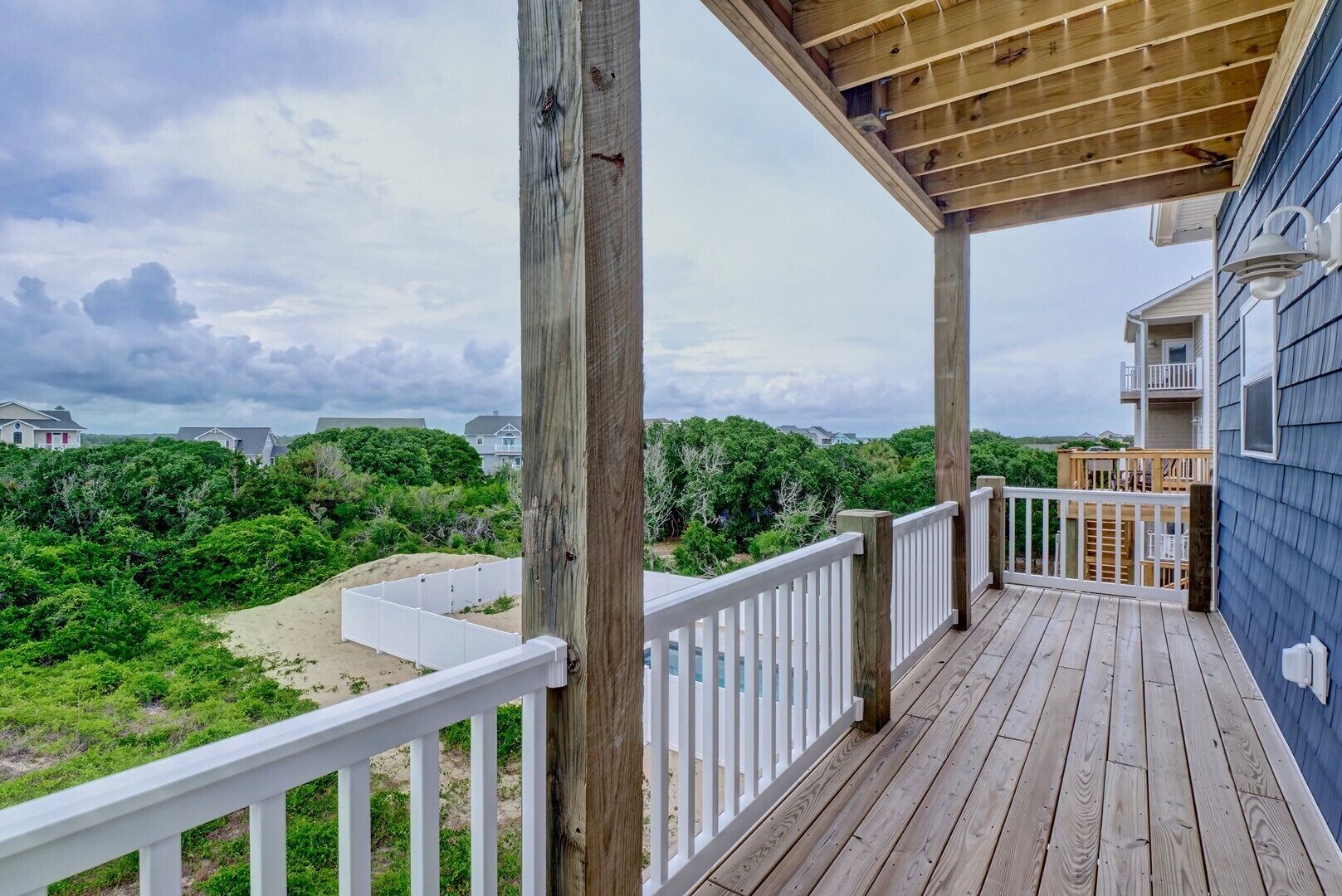 A wooden deck with a white railing overlooking a beach and houses.