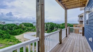 Eine Holzterrasse mit weißer Geländer, mit Blick auf einen Strand und Häuser.