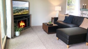 Ein Wohnzimmer mit Kamin, Fernseher, einer Couch und einem Fenster mit Vorhängen.
