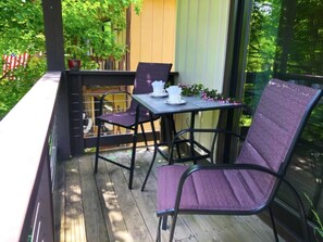A wooden deck with a table and two chairs, a small potted plant, and a window with a view of trees. - Beech Mountain Retreat With Mountain View<br> (Beech Mountain)