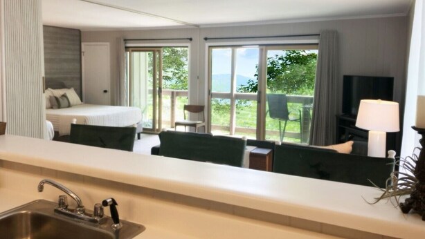 Ein Hotelzimmer mit Bett, Schreibtisch, Stuhl, Fernseher und einem Balkon mit Ausblick ins Freie.