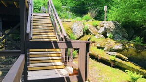 Eine Holztreppe führt zu einem Gebäude mit Metallgeländer, umgeben von üppiger Vegetation und Felsen.