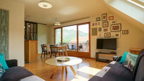 Un salon moderne avec un canapé, une table ronde et un balcon offrant une vue sur les montagnes.