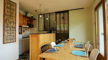 Zona pranzo con tavolo in legno apparecchiato per quattro, sedie bianche e una cucina sullo sfondo.