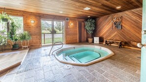 Interior de madera con bañera de hidromasaje, plantas en macetas y vistas al exterior.