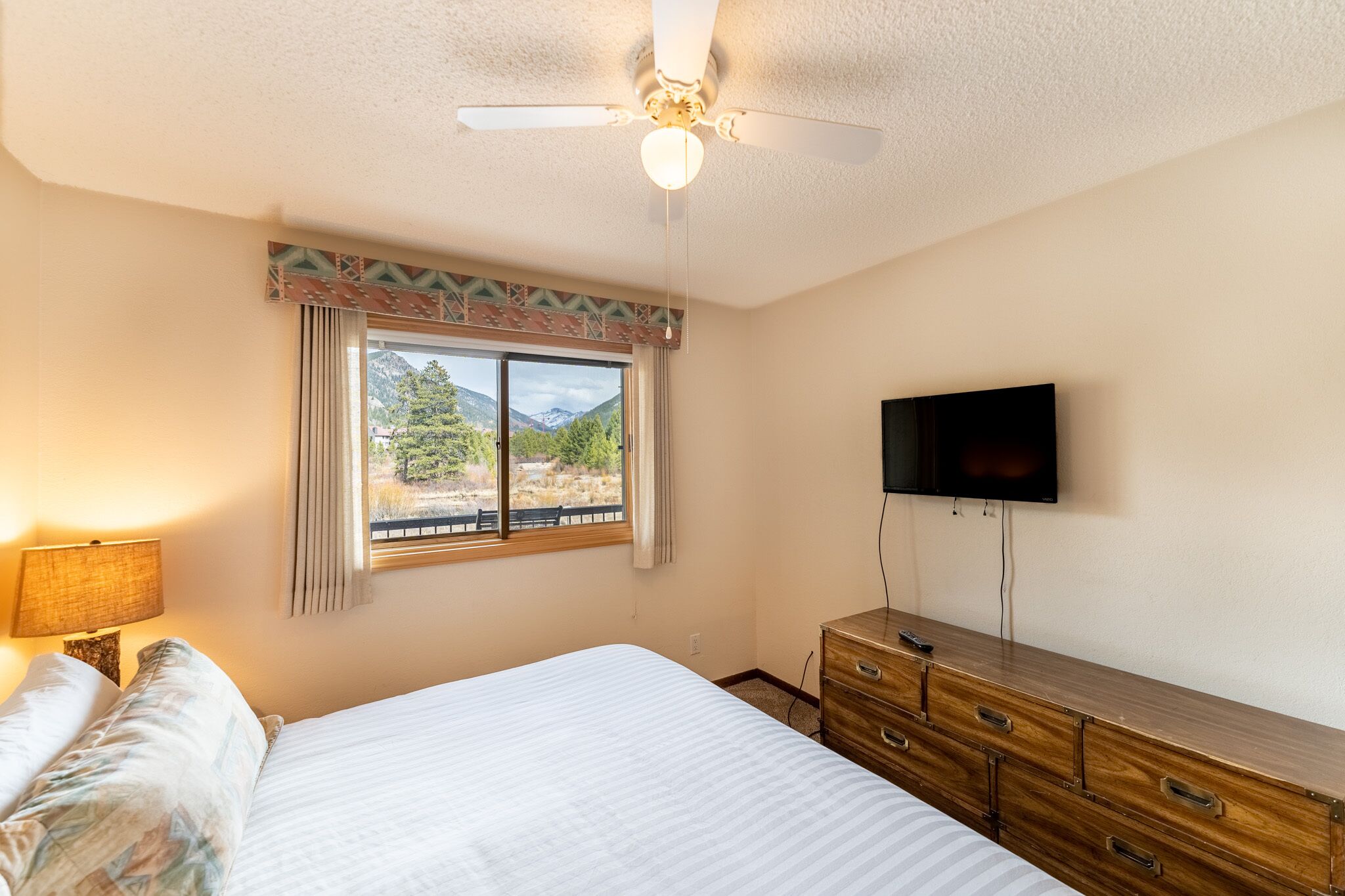 Une chambre à coucher comprenant un lit, une commode, un ventilateur de plafond, un téléviseur et une fenêtre donnant sur les montagnes.