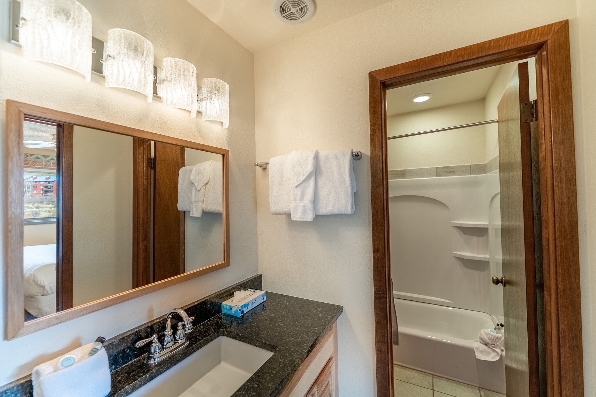 A bathroom with a large mirror, a sink, a shower, and a towel rack.