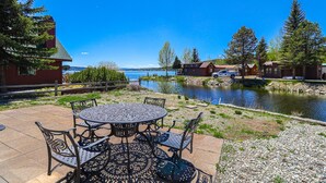 A patio with a round table and chairs, a small pond, and houses in the background. - Edgewater Vista - Waterfront home, sleeps 6, short drive or walk to town! (Grand Lake)