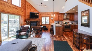 A spacious living area with a fireplace, wooden flooring, and a large TV. - Edgewater Vista - Waterfront home, sleeps 6, short drive or walk to town! (Grand Lake)