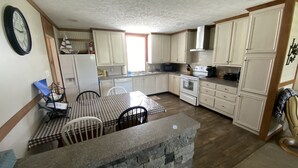 Una cocina con armarios blancos, encimera de piedra, una mesa de comedor con sillas y un reloj en la pared.
