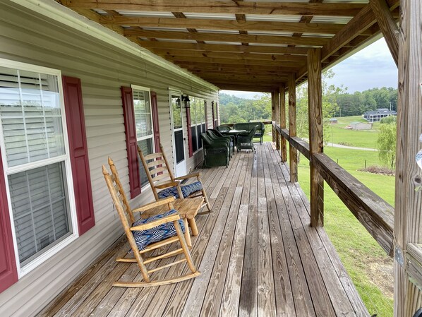 A covered porch with wooden flooring, rocking chairs, and a view of a green landscape.