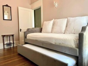 A bed with a pull-out desk, a small table, and a mirror on the wall.
