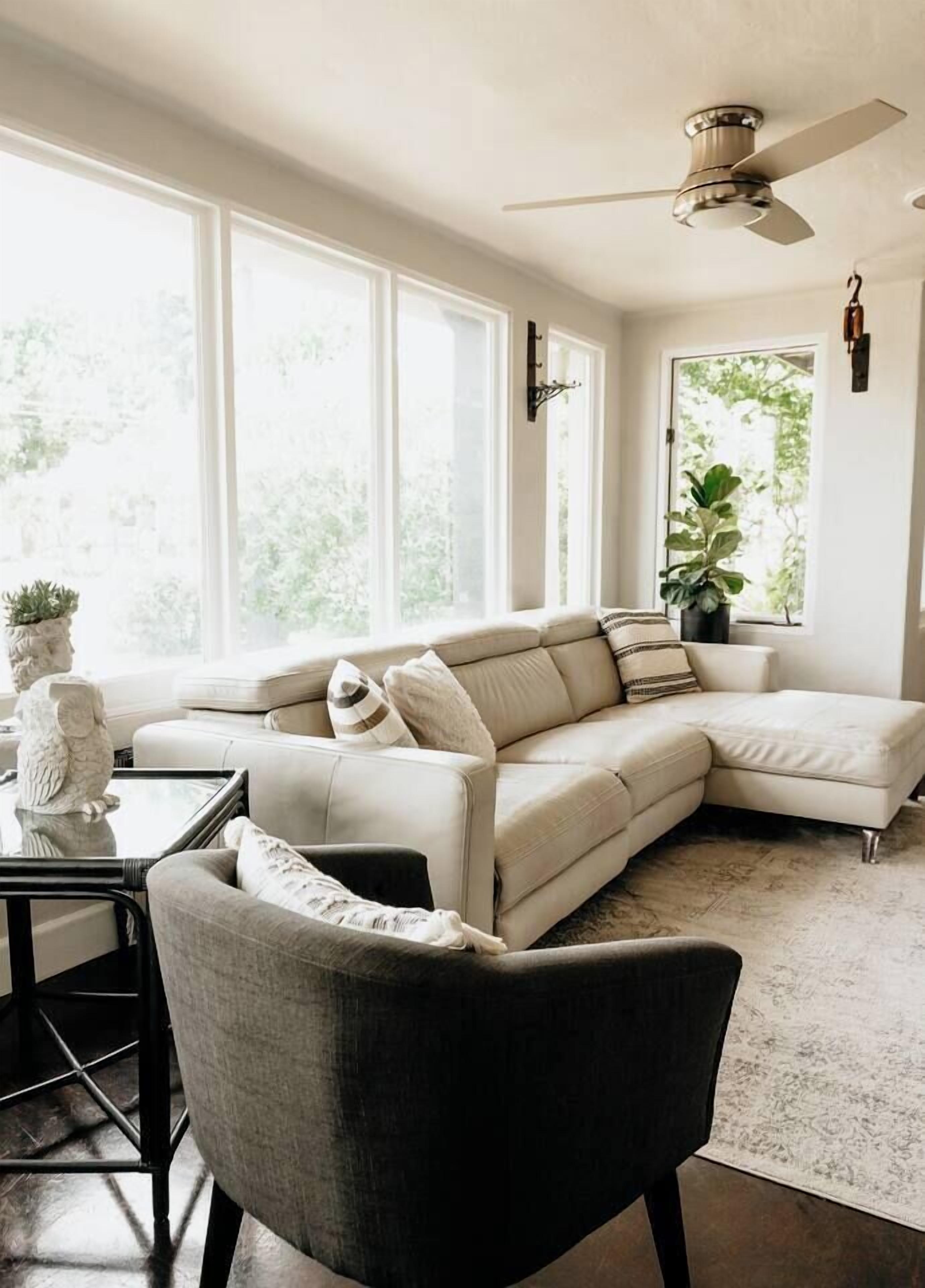 A modern living room with a sectional sofa, a black armchair, a coffee table, and a ceiling fan.